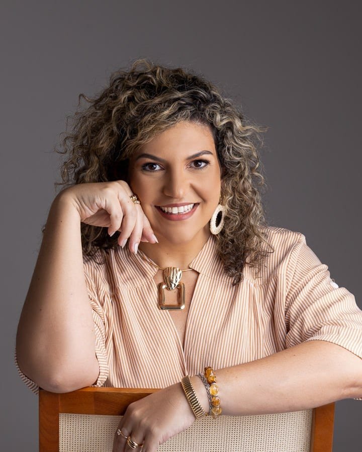 Mariana Marco, psicóloga, sorrindo, apoiada no encosto de uma cadeira.